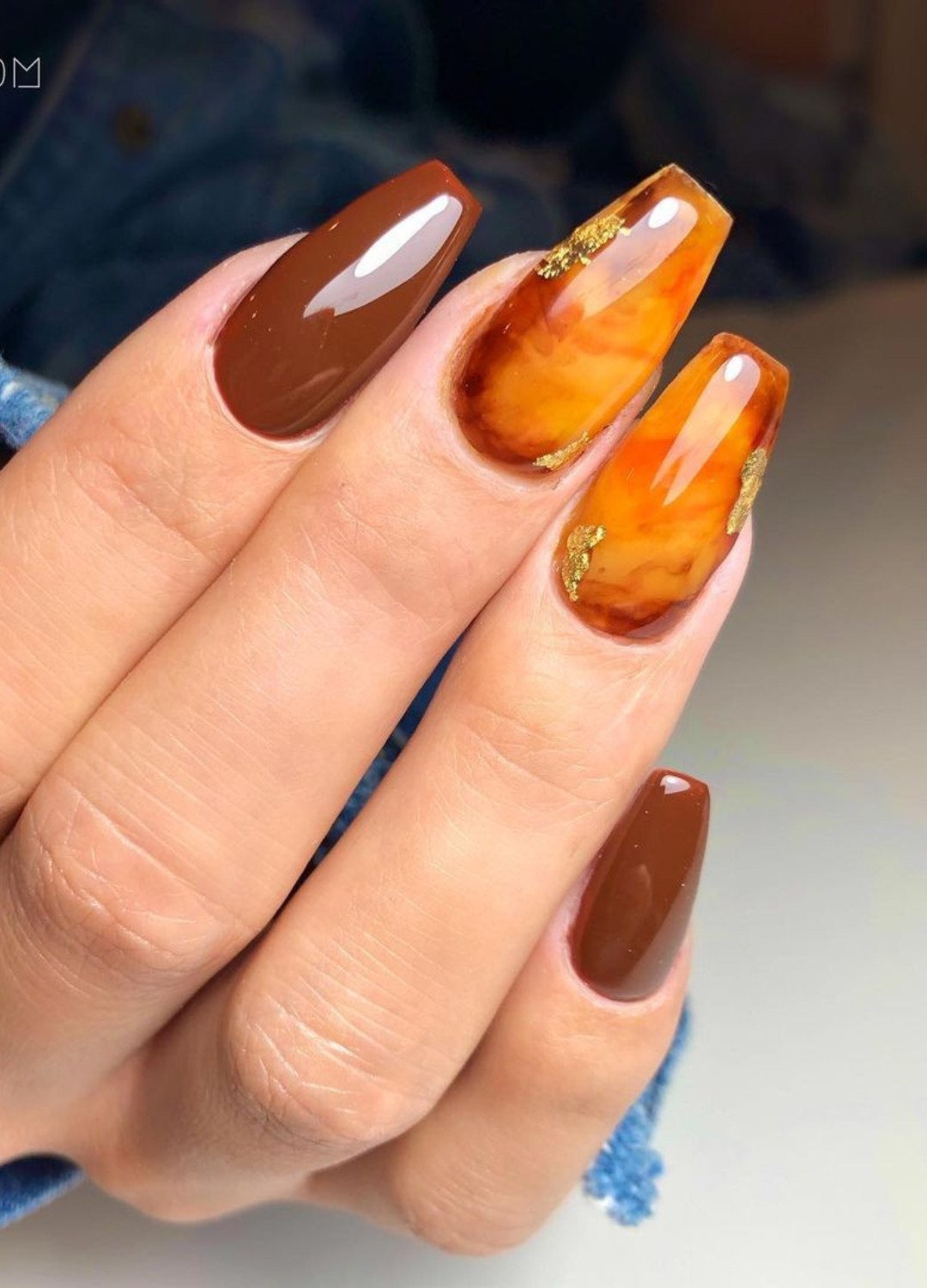 hand showing Burnt orange nails with Hue and golden foil pattern