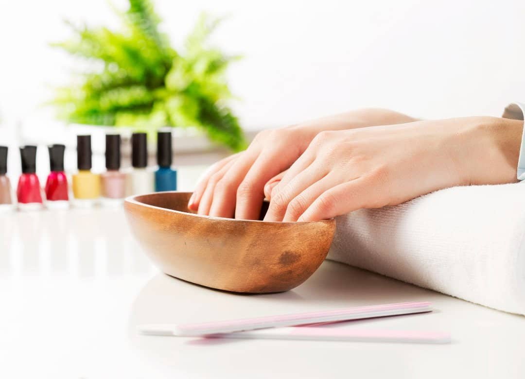 Hands soaking in a wooden bowl as part of a nail care routine at home — first step in prepping nails for trimming, cuticle care, and hydration.