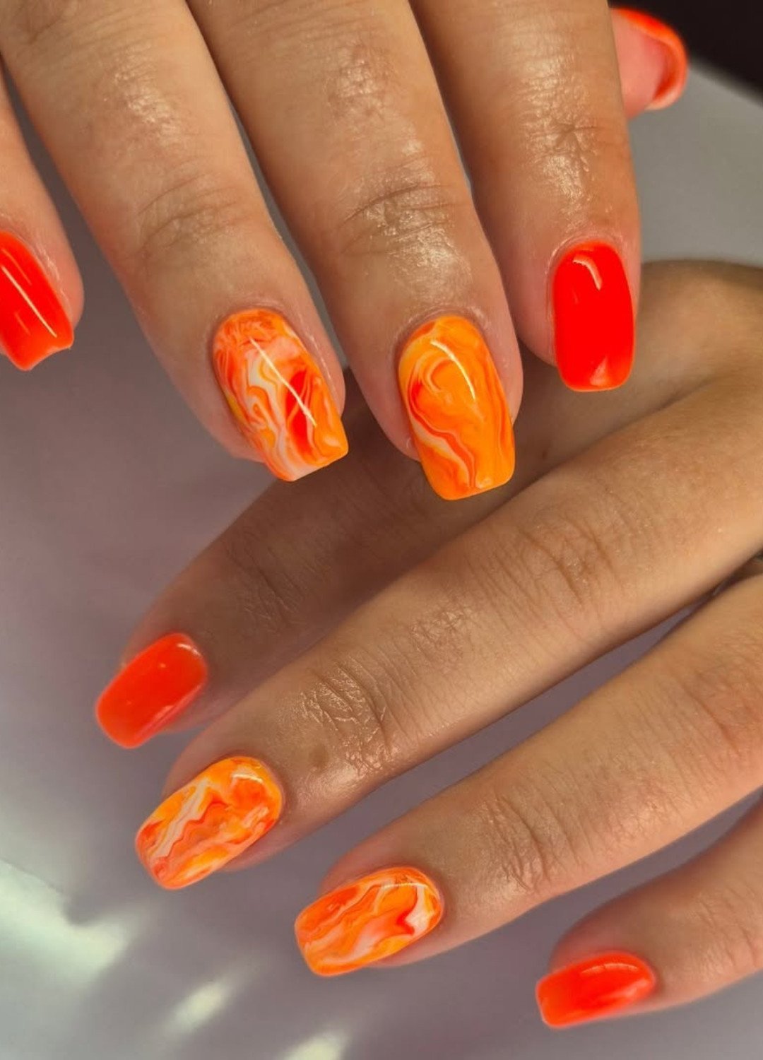 hand displaying orange clementine shades and flame-like swirls marble nail art design
