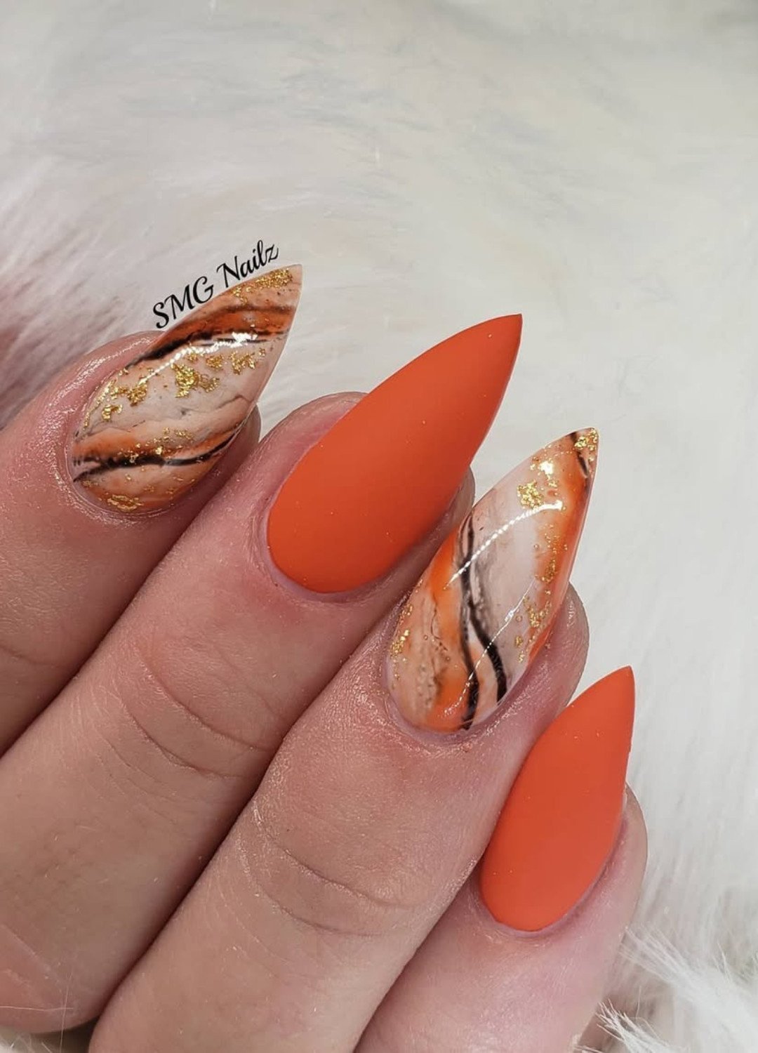 Matte orange nails already feel elevated, but pair with a glossy sprinkle of gold flakes on a mix of orange, black and off-white flamy base accents,