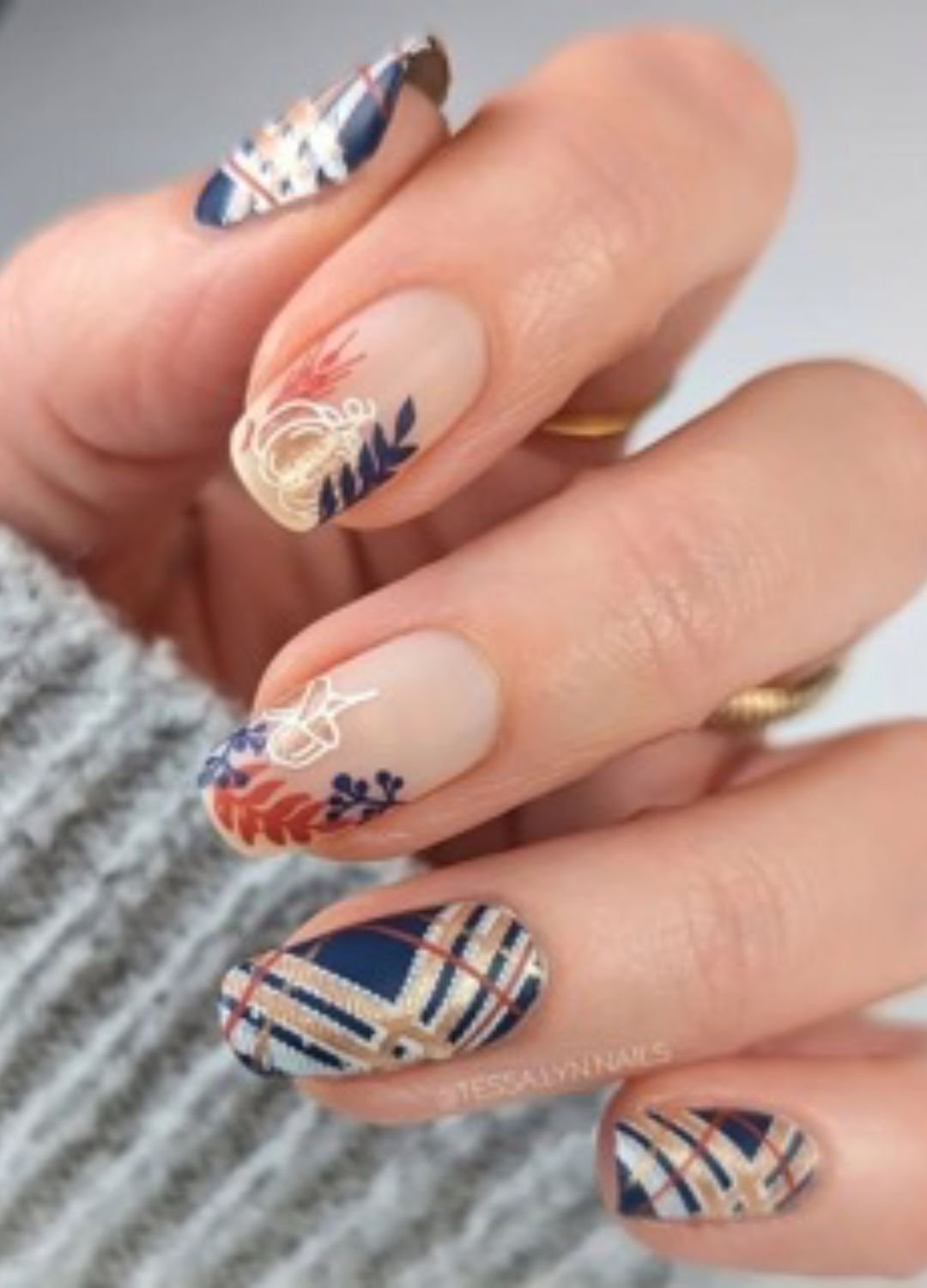 Image of one of the thanksgiving nail ideas featuring blue, burgundy, golden, and rustic orange stripes layered, and on the other hand, a neutral base with festive fall leaves and pumpkin